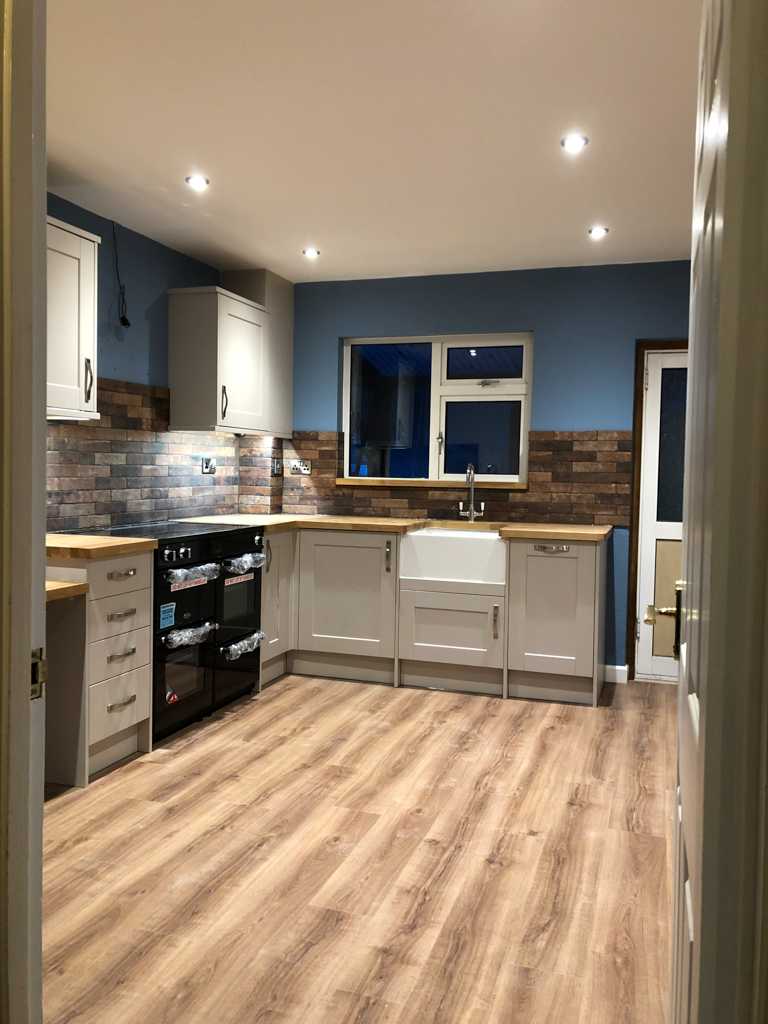 A kitchen with blue walls and wood floors. Off white cabinets and oak worktops.